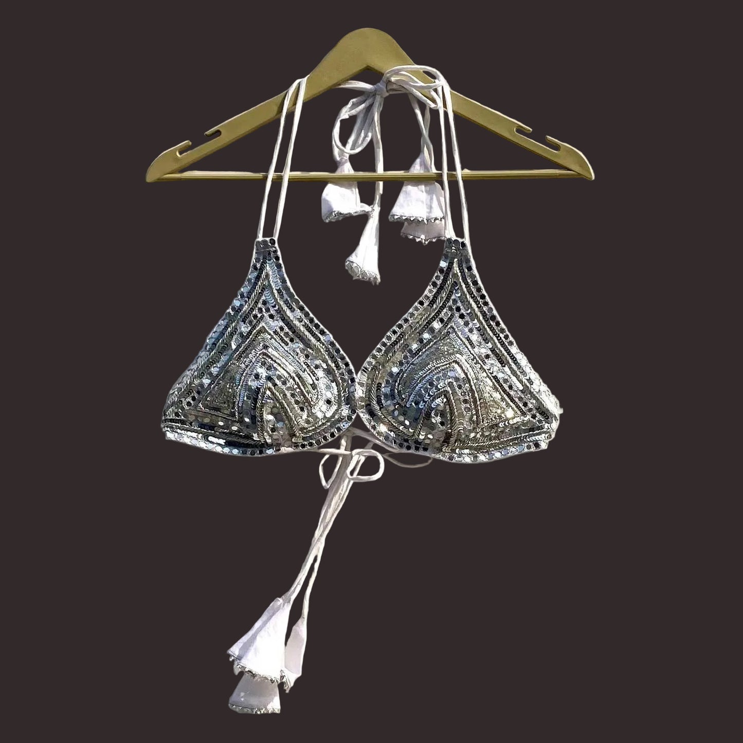 Silver bralette with intricate patterns on a hanger against a white background